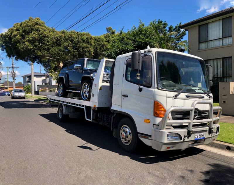 Black 4WD loaded on a white tilt-tray tow truck on a suburban street