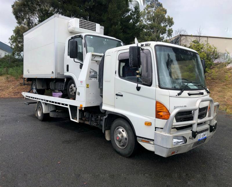 Refrigerated box truck being transported on a white tilt-tray truck