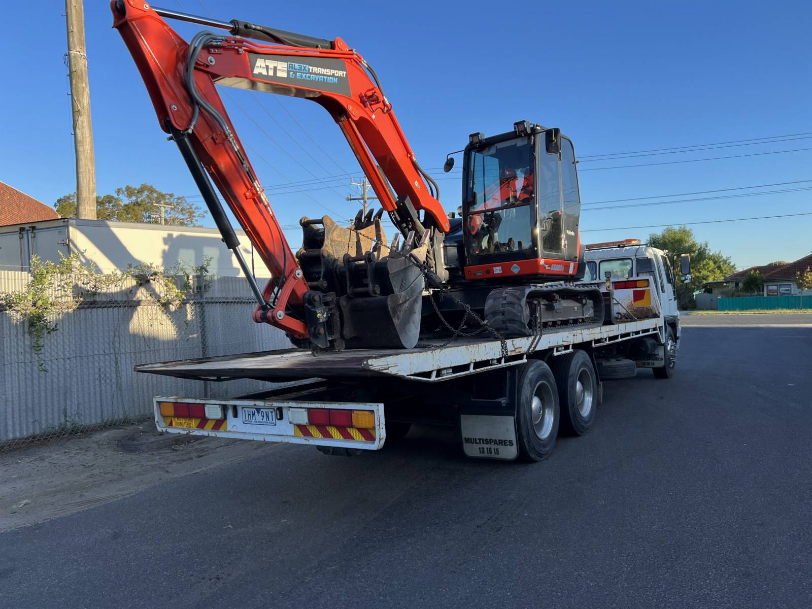 Mini excavator chained down on a tilt-tray truck for machinery transport