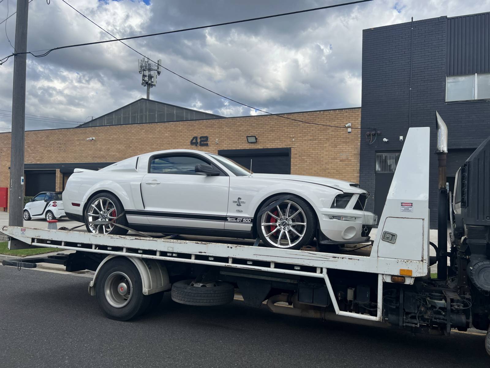 White muscle car being transported on a tilt-tray truck