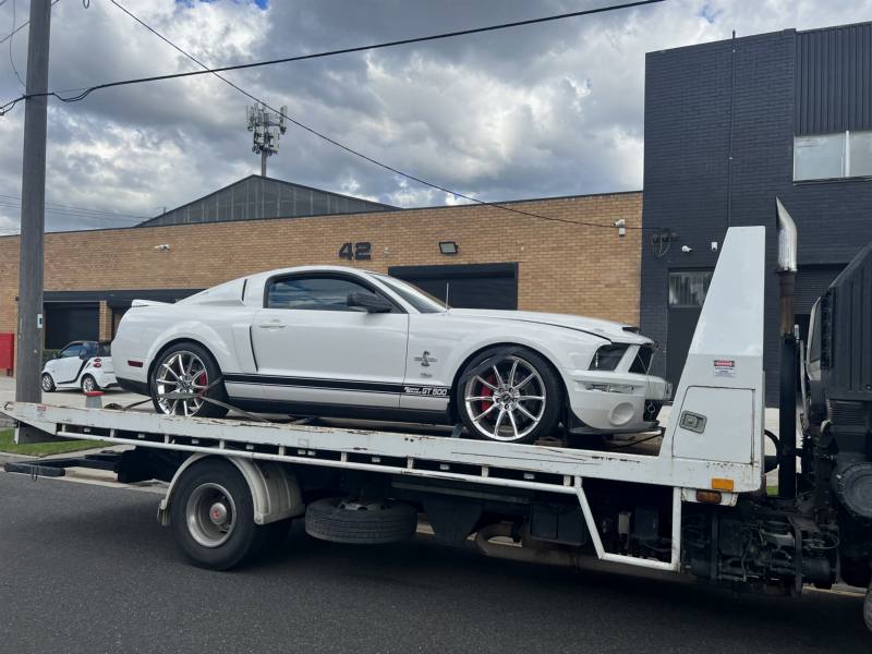 White muscle car on a tilt-tray tow truck in an industrial street